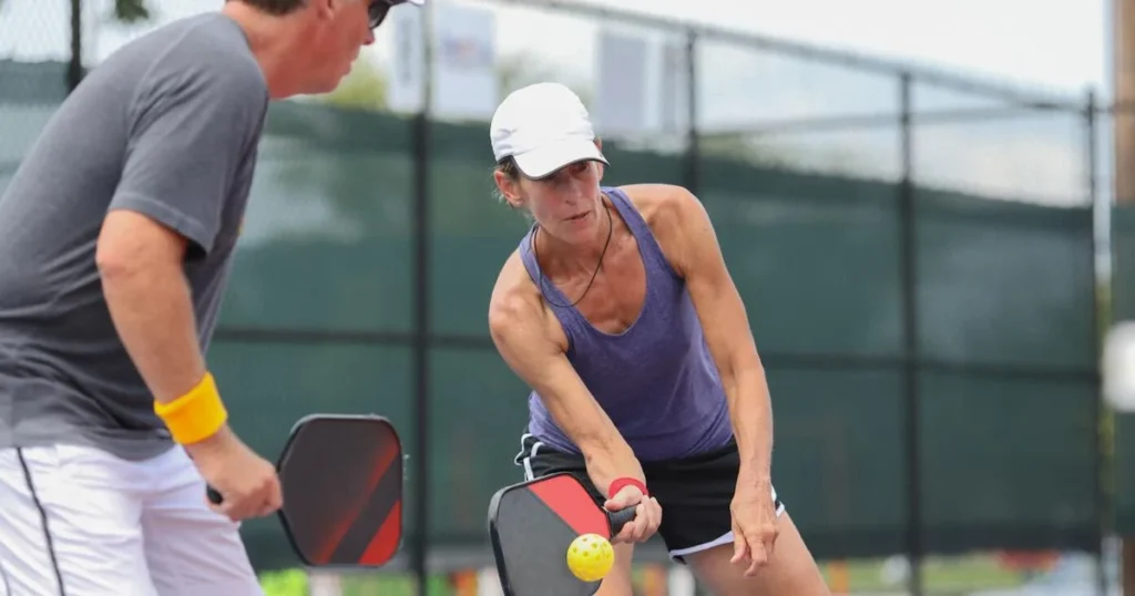 A man and woman engage in a lively ping pong match on a tennis court, showcasing their skills as a funny pickleball team.