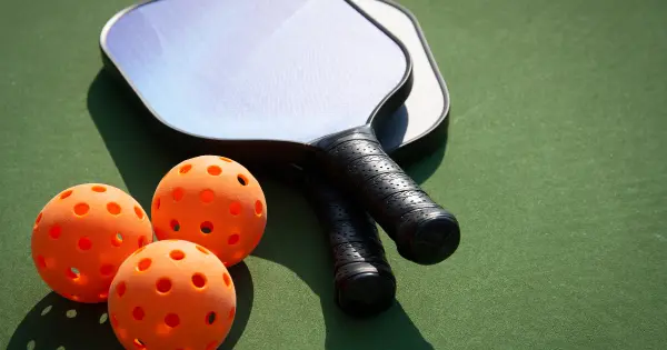 A paddleball and two tennis balls resting on a green surface, illustrating the playful essence of pickleball slang.
