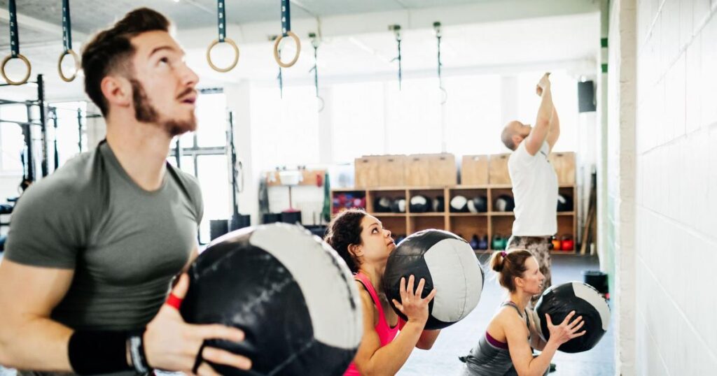 A diverse group of individuals engaged in a vigorous CrossFit workout at a gym, showcasing teamwork and fitness enthusiasm.